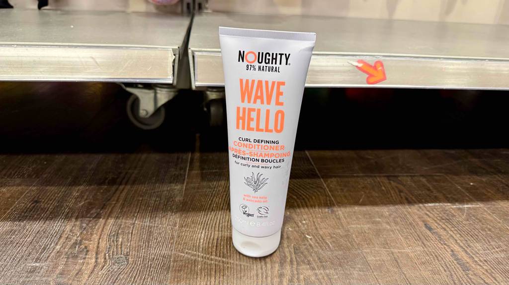Eine weiße Tube mit Locken-Conditioner im Test steht vor einem Regal mit Rollen.