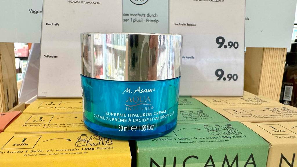 Im Test: Die M.-Asam-Gesichtscreme im hellblauen Tiegel mit silberfarbenem Schraubverschluss steht auf mehreren Seifenpackungen im Drogeriemarkt.