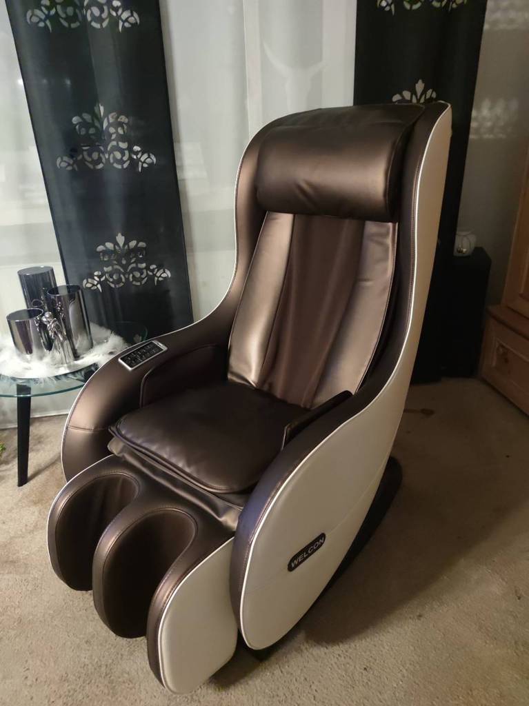 Massagesessel im Test: braunes Modell im Leder-Design steht in einem Wohnbereich auf beigefarbenem Teppichboden vor einem Fenster.