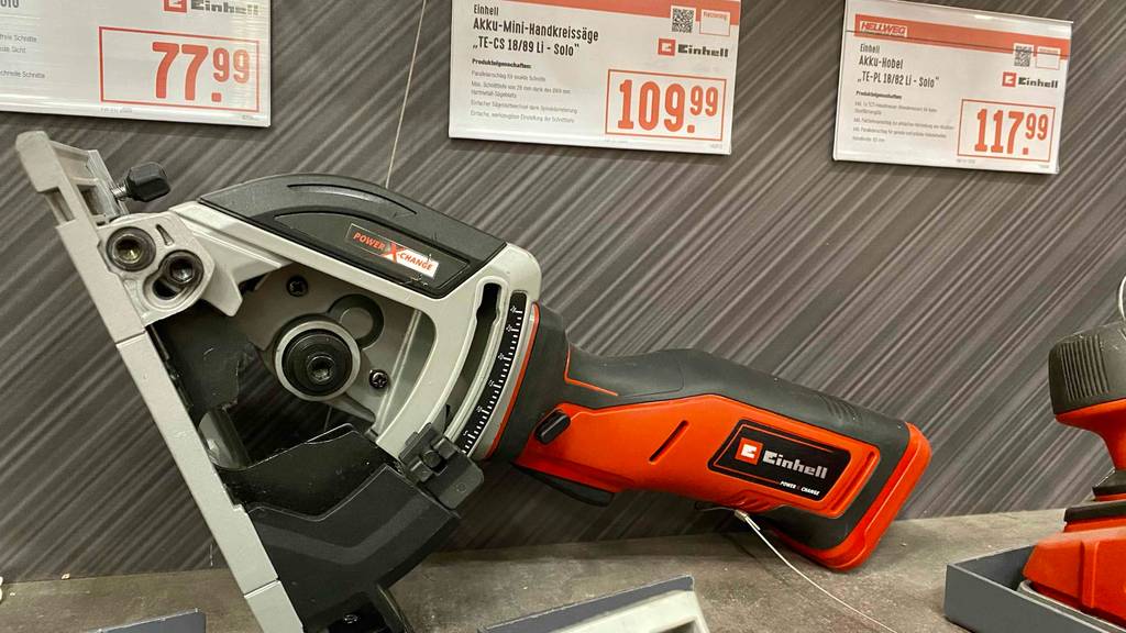 Mini-Handkreissäge im Test: Seitenansicht auf ein grau-rotes Einhell-Modell inklusive Parallelanschlag auf einem Ausstellungsregal mit Preisschildern.