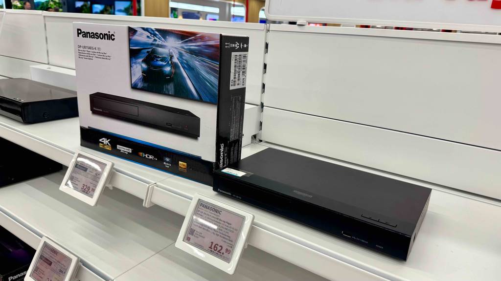 HD-Receiver-Test: Neben einem schwarzen, ausgestellten Receiver steht eine Produktpackung der Marke Panasonic auf einem weißen Regal mit Preisschildern.