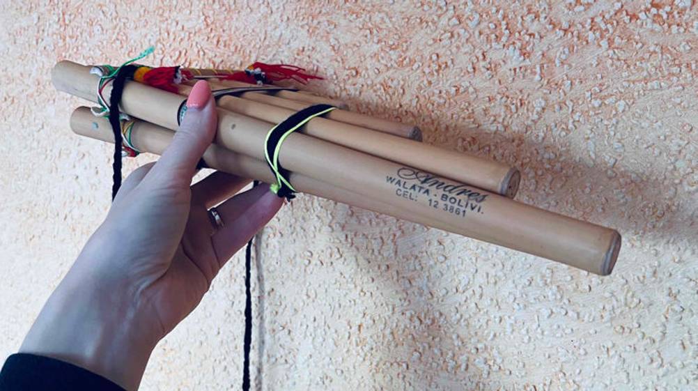 Hand hält Panflöte im Test, mit Markenzeichen Andres aus Walata-Bolivi, vor Raufasertapete.