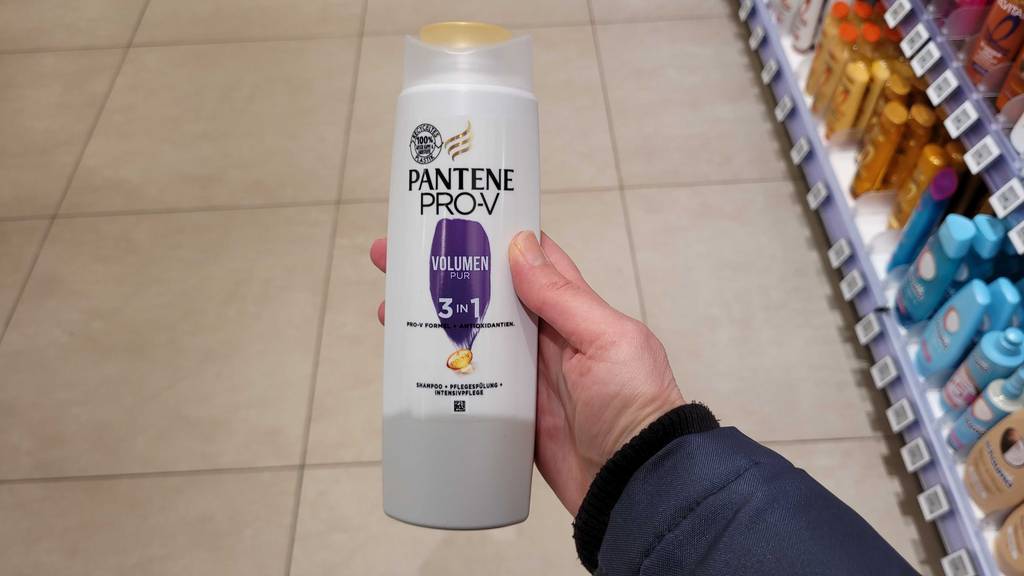 Pantene-Pro-V-Shampoos im Test: Eine Hand hält eine Quetschflasche über dem Boden in einem Drogeriemarkt.