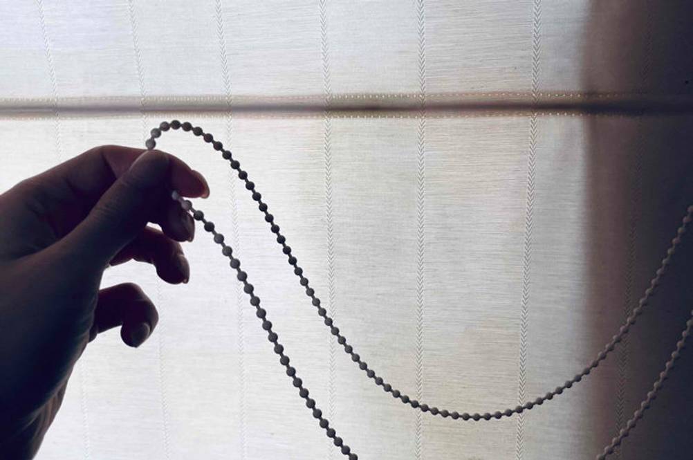 Raffrollo-Test: Hand hält Kordelzug eines hellen Raffrollos.