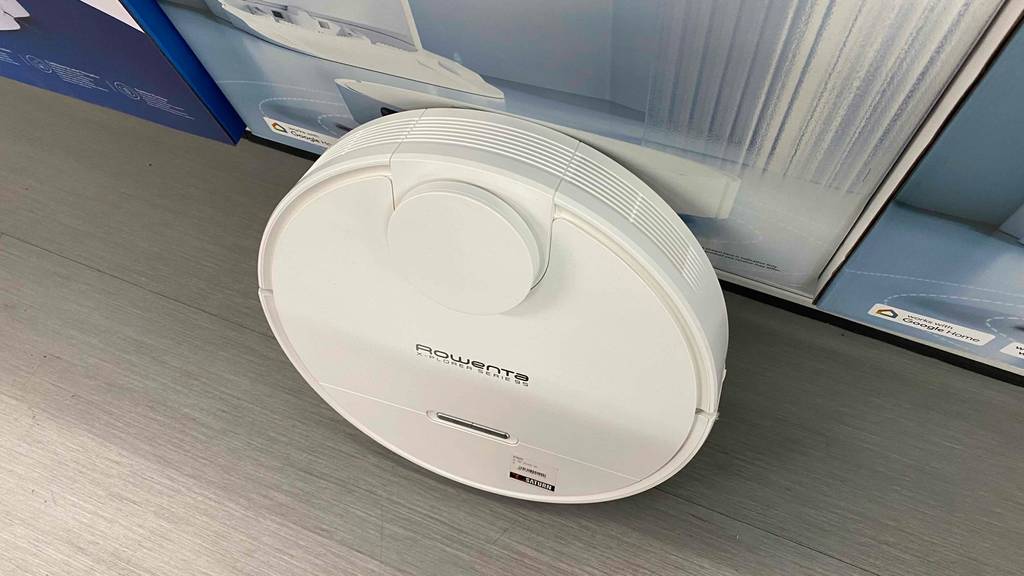 Rowenta-Saugroboter-Test: Ein kompakter, weißer Rowenta-Saugroboter ist aufrecht auf seinem schmalen Rand vor seiner Verpackung im Geschäft ausgestellt.