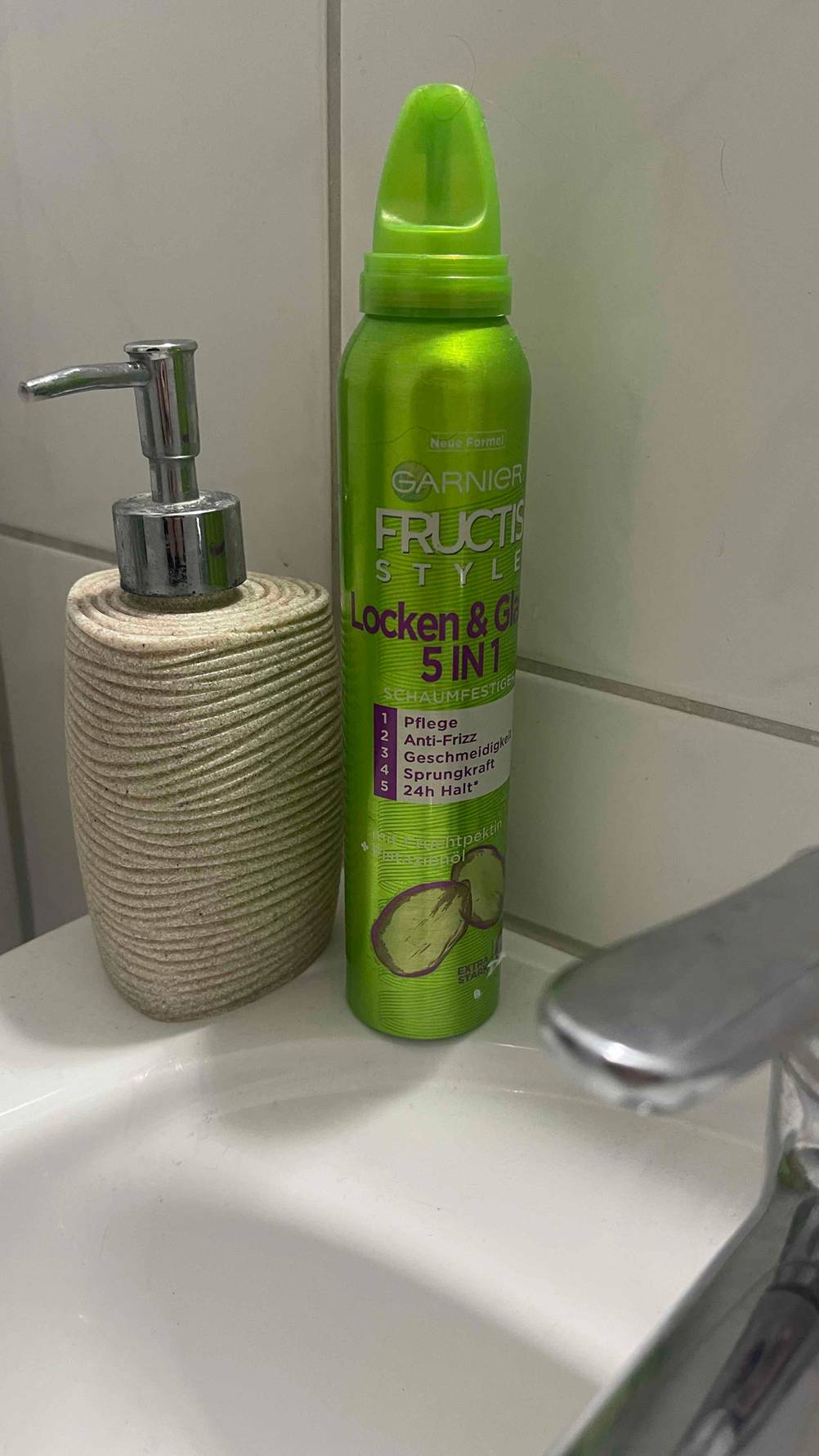 Im Test: Der Schaumfestiger für Locken befindet sich innerhalb seines giftgrünen Spenders neben einem Seifenspender auf dem Waschbecken.