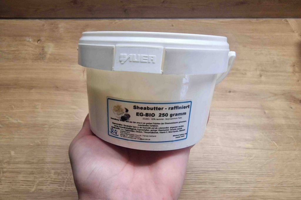 Sheabutter-Test: Hand hält 250-Gramm-Plastikdose mit raffinierter Sheabutter hoch.