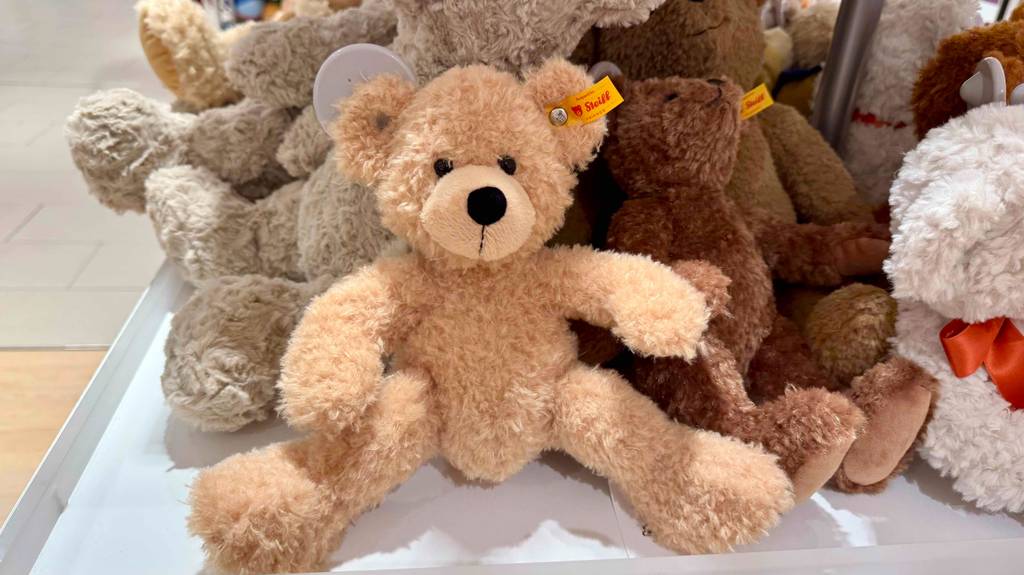 Mehrere Steiff-Teddys im Test sitzen nebeneinander auf einem weißen Regal im Geschäft.