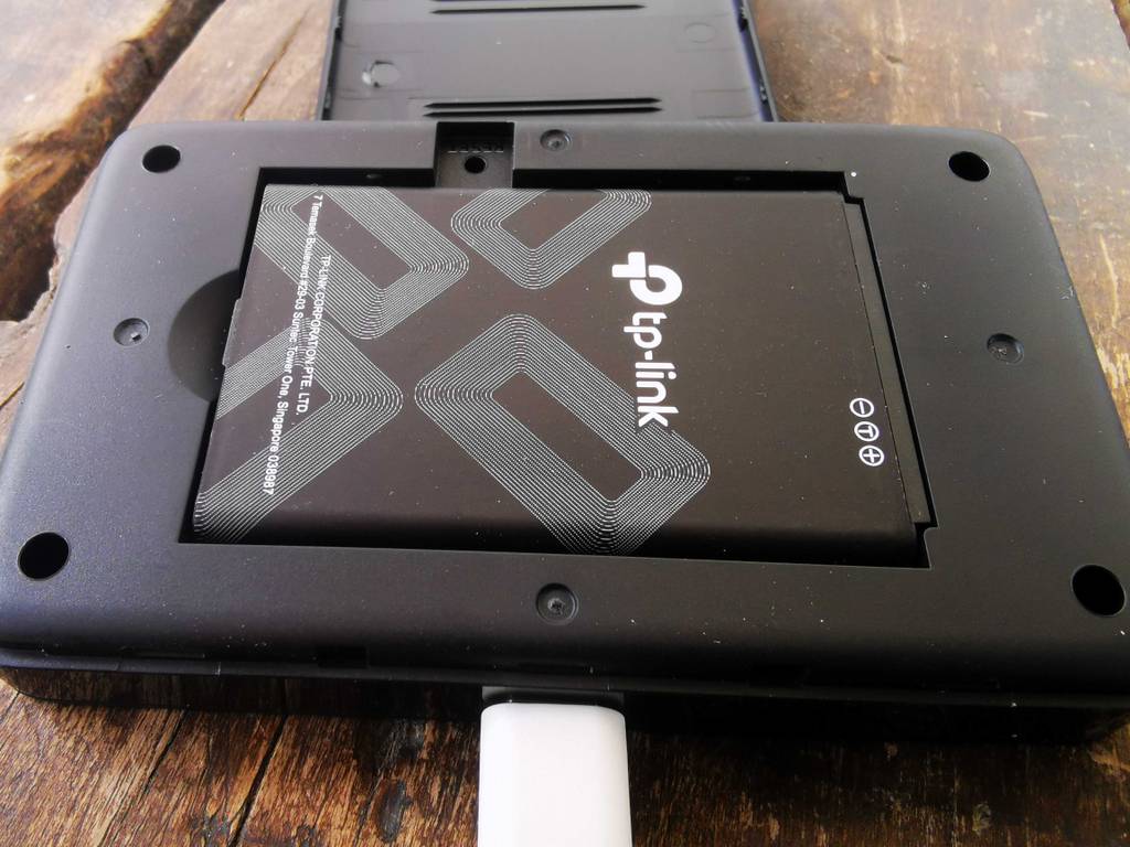 Der schwarze getestete TP-Link-Router liegt geöffnet, mit Fokus auf der integrierten Batterie auf einem Holztisch.