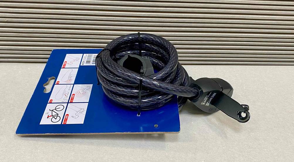 ABUS-Fahrradschloss im Test: ein schwarzes Spiralkabel-Schloss liegt aufgerollt auf einer blauen Verkaufspappe auf einer hellgrauen Fläche.