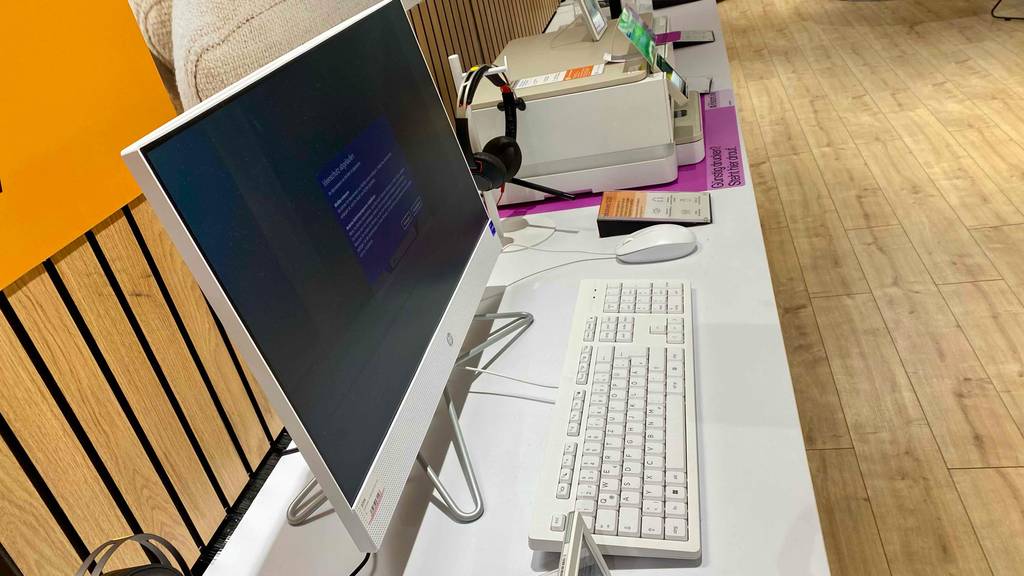Weißer All-in-One-PC im Test befindet sich neben einem weißen Drucker auf einem weißen Ausstellungstisch in einem Geschäft.