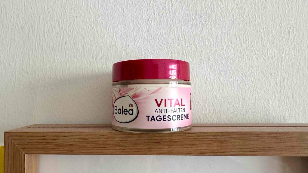Die getestete Balea-Tagescreme im Tiegel steht auf einem Holzregal vor einer weißen Wand.