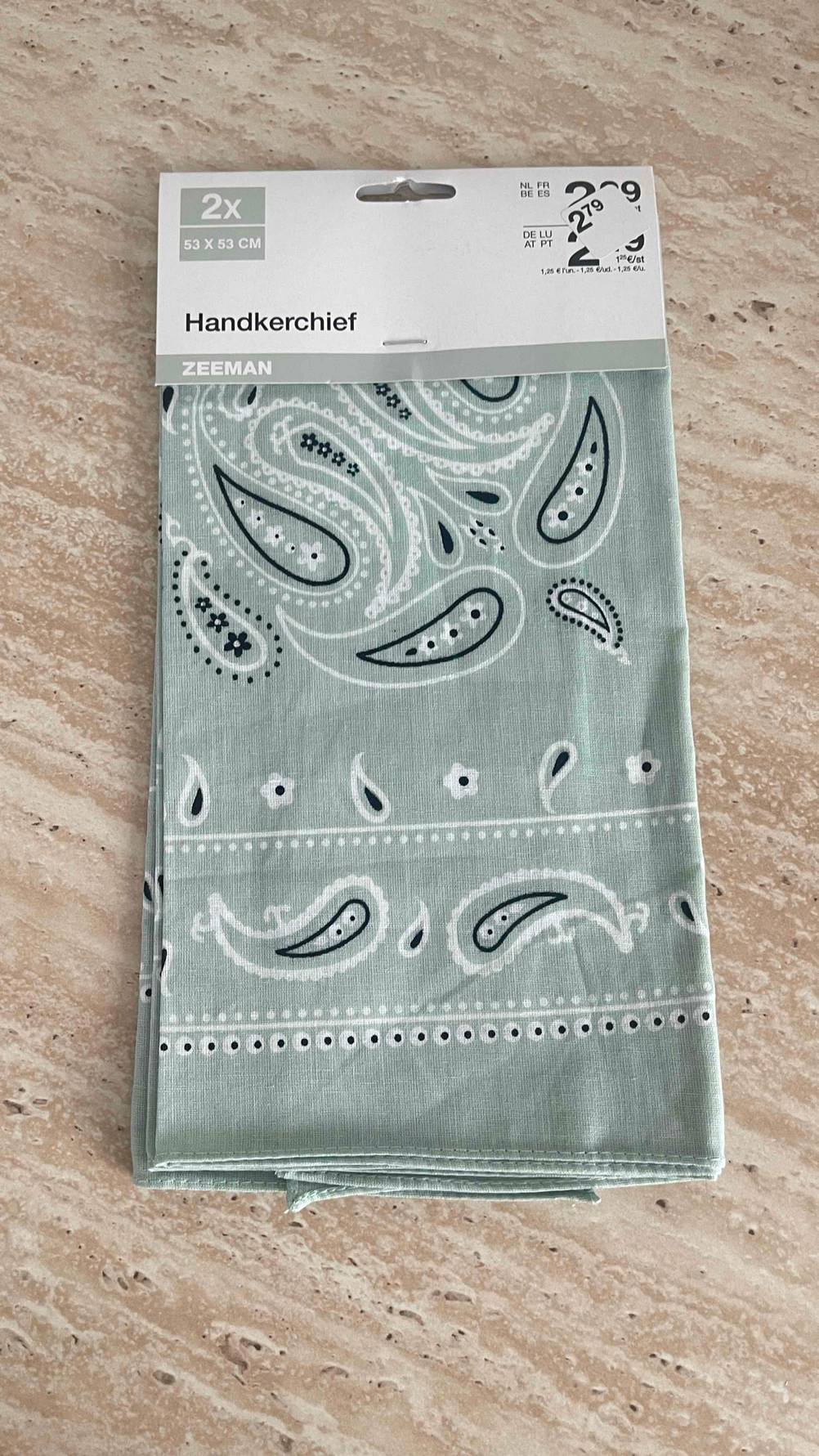 Das getestete Bandana in Grau liegt in einem Zweier-Pack auf einem Holztisch.