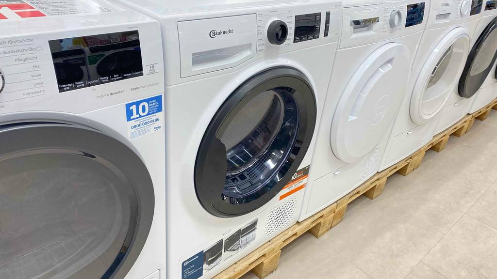 Wärmepumpentrockner-8-kg-Test: weißer Bauknecht-Wärmepumpentrockner mit schwarz umrahmter Vorder-Tür steht in einem Verkaufsbereich zwischen weiteren Frontladern.