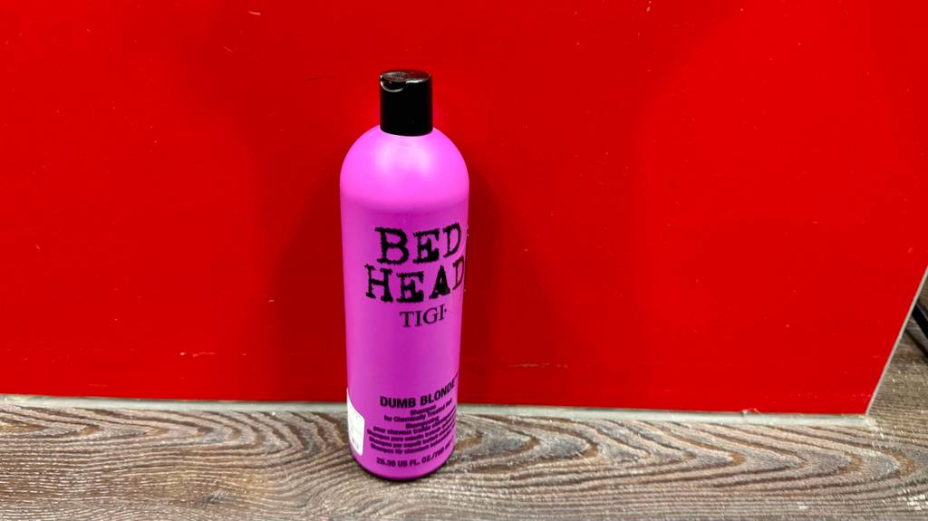 Im Test: Das Bed-Head-Shampoo in der pinken Quetschflasche steht vor einem roten Hintergrund.