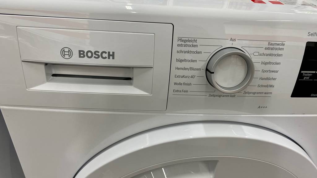 Wärmepumpentrockner-8-kg-Test: Detailansicht des Bedienbereichs mit Waschpulver-Schublade und Programmwahl-Drehknopf eines weißen Modells der Marke Bosch.