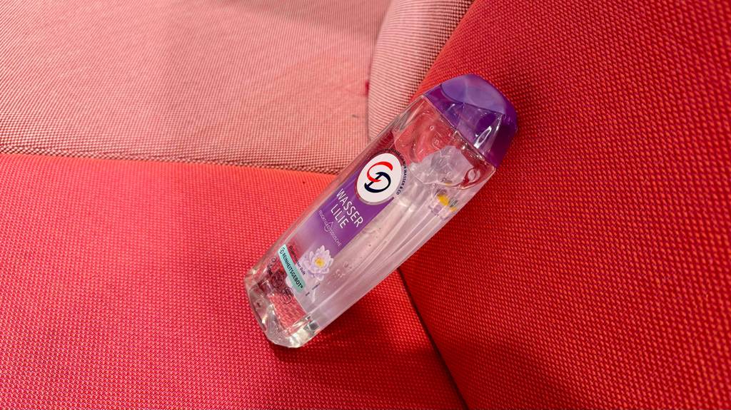 Ein getestetes CD-Duschgel in der transparenten Quetschflasche liegt auf einem roten Autositz.