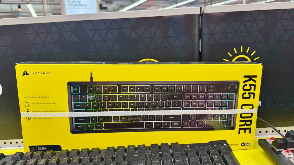 Im Test: Die Corsair-Tastatur inklusive beleuchteter Tasten befindet sich in einer gelben Verpackung hinter der schwarzen Tastatur auf dem Ausstellungsregal.