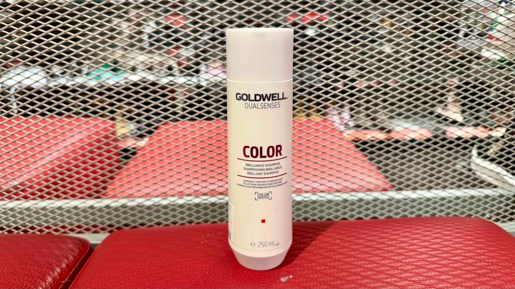 Eine weiße Kunststoffflasche mit getestetem Goldwell-Shampoo steht auf einem roten Hocker im Geschäft.