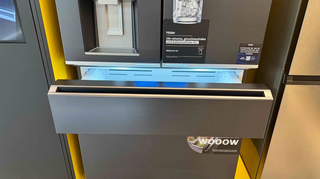 Der zweitürige Kühlschrank Haier-Side-by-Side im Test steht mit geöffneter Schublade in einem Ausstellungsbereich.