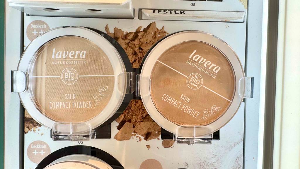 Mehrere Dosen mit Naturkosmetik-Make-up der Marke Lavera stehen auf einem Verkaufsregal neben Testern.
