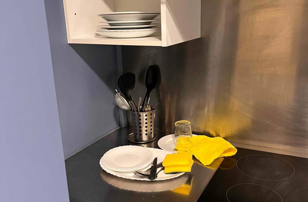 Miniküchen-Test: Über der Aluminiumarbeitsplatte mit abgestelltem, weißen Geschirr befindet sich ein weißer Geschirrschrank.