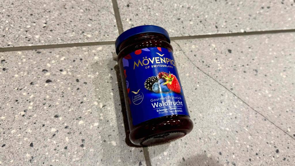 Ein Glas mit getesteter Mövenpick-Marmelade Waldfrucht liegt auf einem Fliesenbelag.