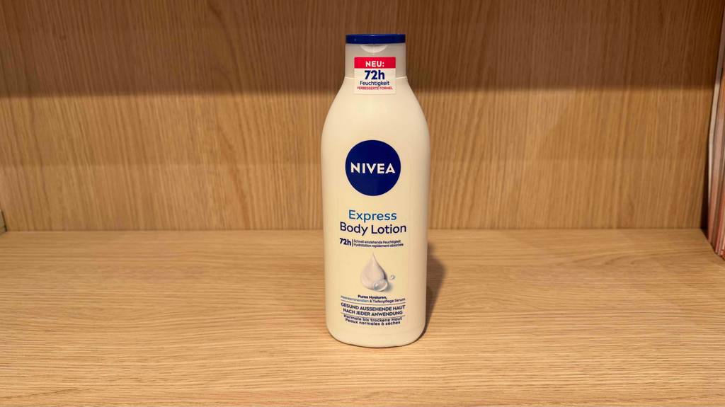 Eine weiße Flasche Nivea-Bodylotion im Test steht auf einem Regal in Holzoptik.