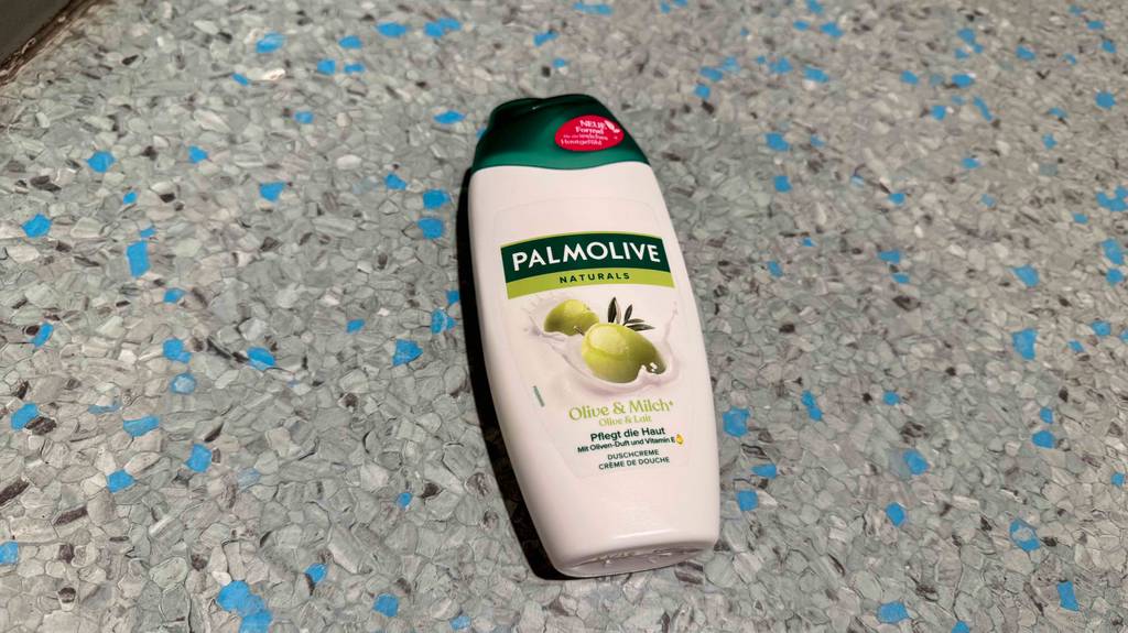 Auf einem Linoleumbelag liegt eine weiße Quetschflasche mit getestetem Palmolive Duschgel.