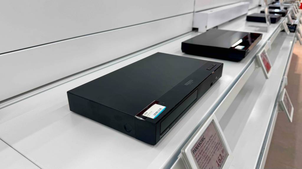 HD-Receiver im Test: Neben einem schwarzen, ausgestellten Receiver stehen weitere schwarze Modelle auf einem weißen Regal mit Preisschildern.