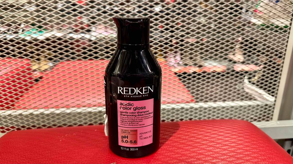 Getestet: Ein Redken-Shampoo in der schwarzen 300-ml-Kunststoffflasche steht auf einer roten Lederoberfläche.