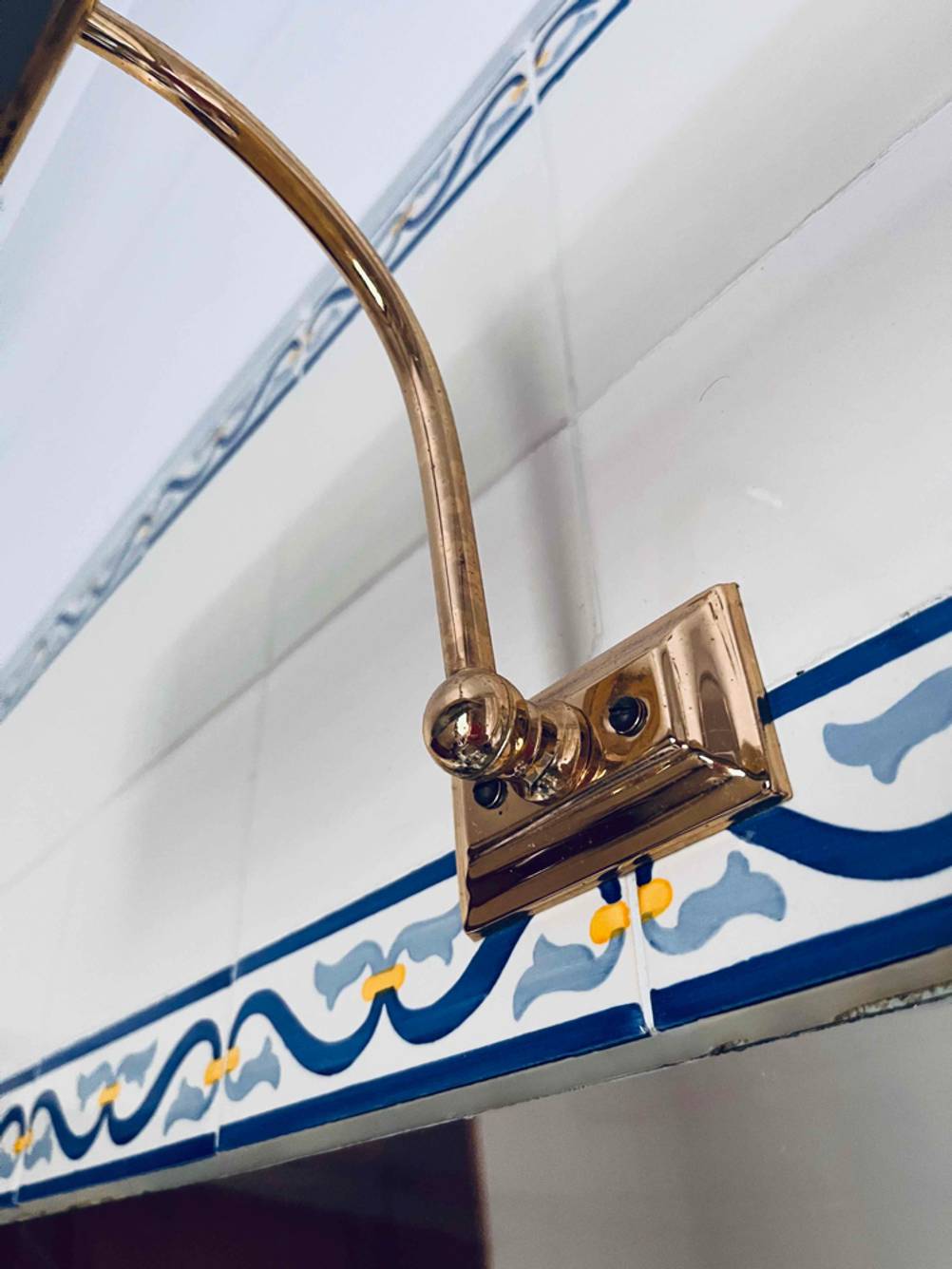 Spiegelleuchte im Test: Detailaufnahme des an der Wand angeschraubten Befestigungselements eines goldenen Messing-Modells.