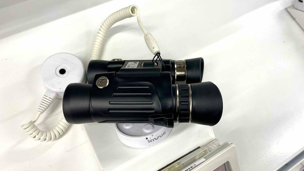 Seitenansicht von einem schwarzen Steiner-Fernglas im Test, das gesichert in einem weißen Ausstellungsbereich liegt.