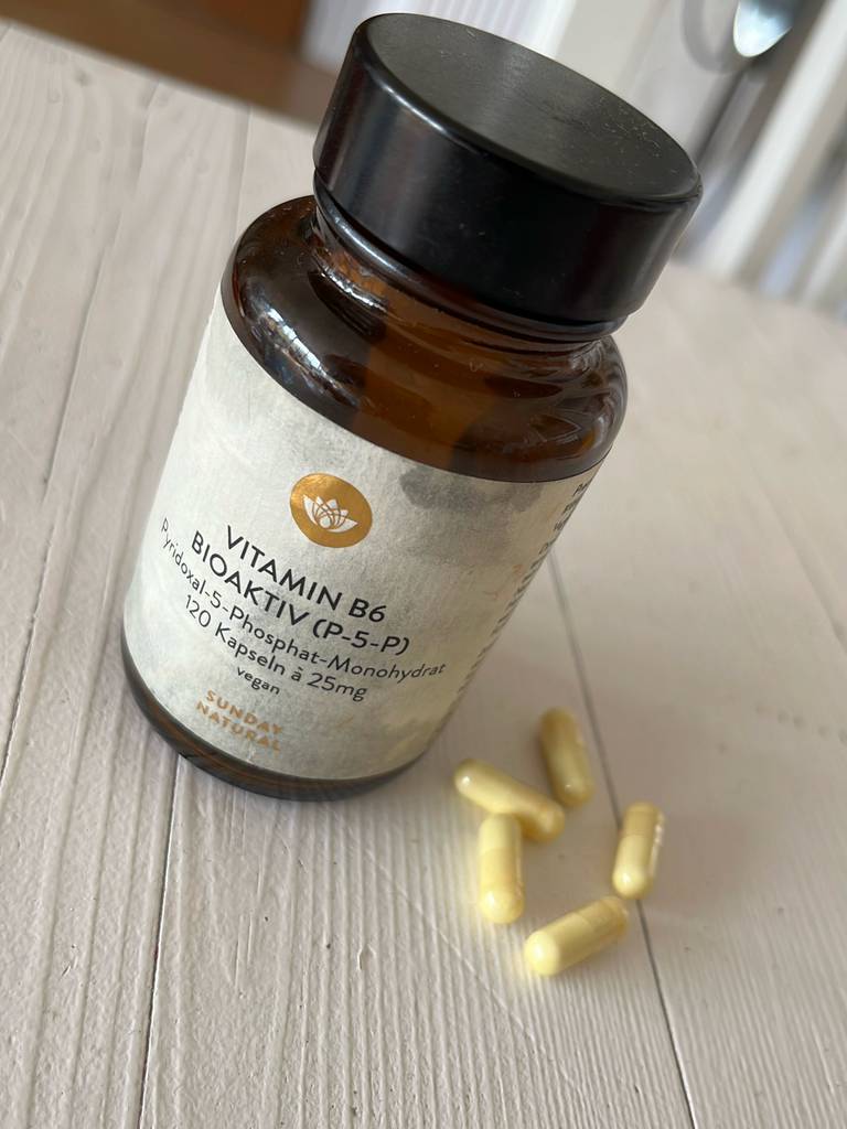Das getestete Vitamin-B6-Präparat in dem braunen Glasbehälter mit 120 Kapseln à 25 mg steht neben einigen gelben Kapseln auf einer weißen Holzfläche.