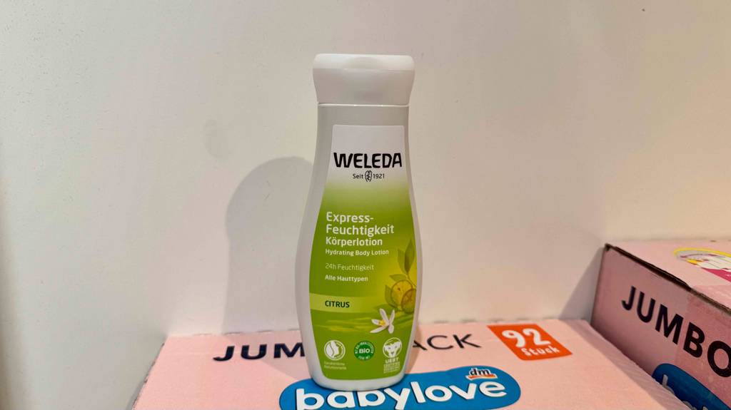 Eine Kunststoffflasche WELEDA Bodylotion im Test steht auf einem pinkfarbenen Karton.