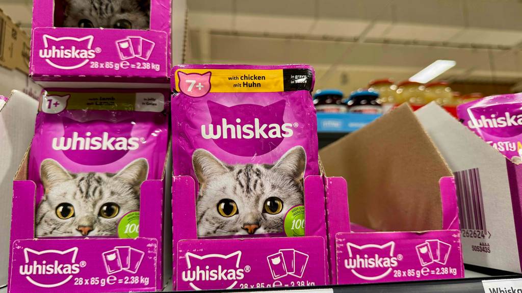 Mehrere pinkfarbene Frischhaltebeutel mit getestetem Whiskas-Nassfutter stehen in Kartons auf einem Verkaufsregal.