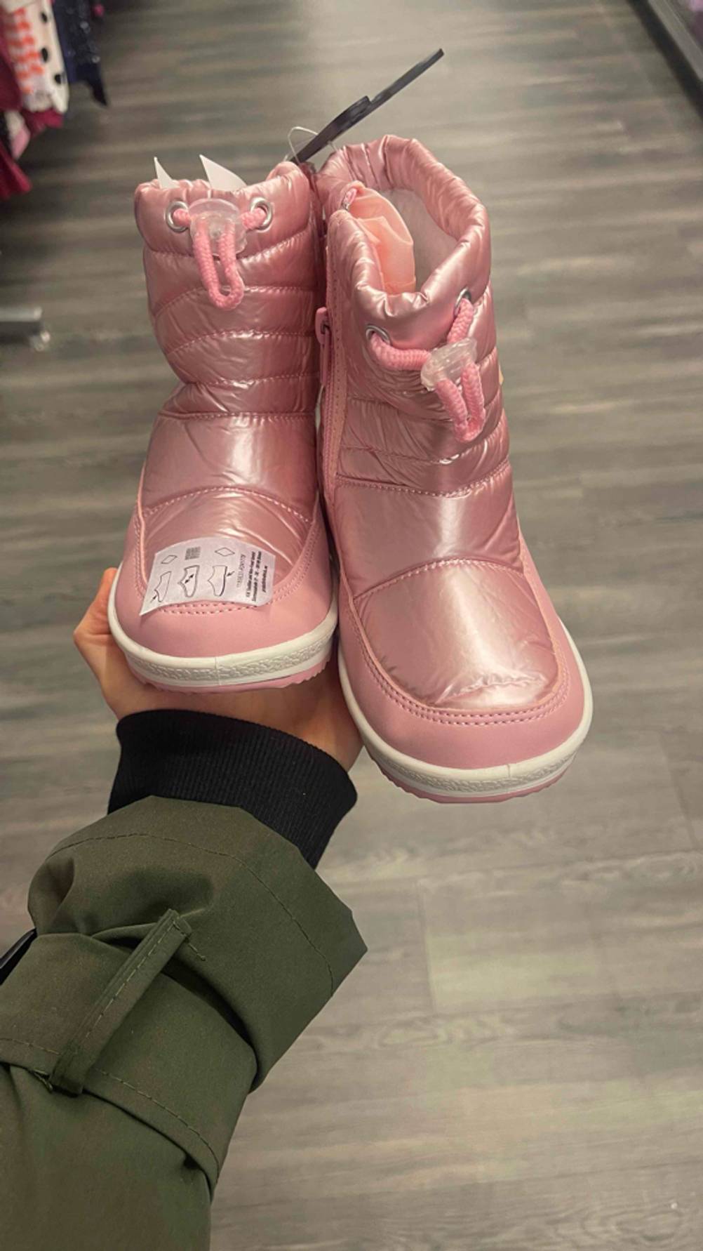 Im Test: Die Winterstiefel für Kleinkinder in der Farbe Rosa stehen auf einer Handfläche im Geschäft.
