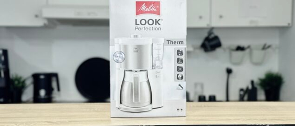 Die Verpackung der Melitta Look V Perfection steht auf einem Tisch. Die Vorderseite mit Modellname und Thermoskanne ist gut erkennbar.