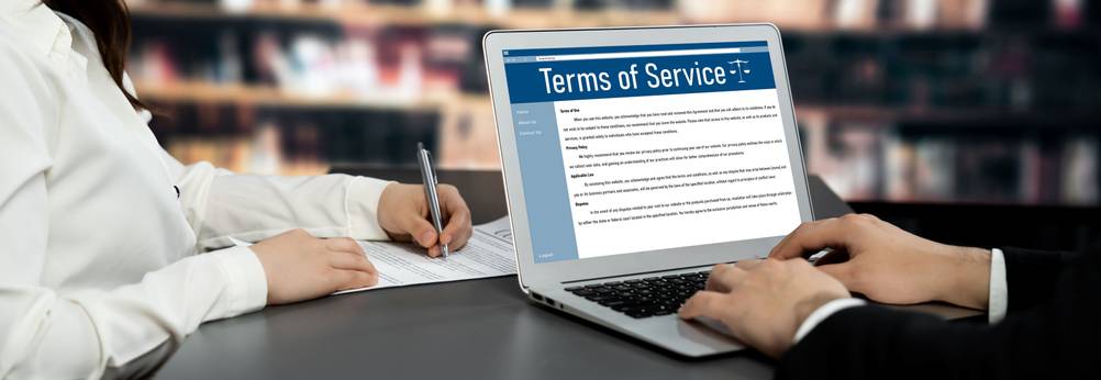 Zwei Personen sitzen an einem Schreibtisch. Die eine Person arbeitet dabei am Laptop, während die andere Dokumente in Papierform bearbeitet.