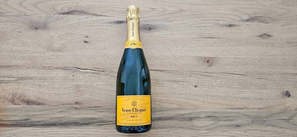 Eine Flasche getesteter Champagner von Veuve Clicquot liegt auf einer Holzfläche.