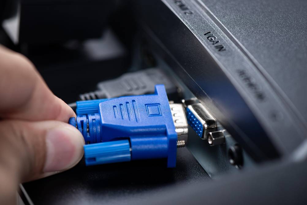 VGA-HDMI-Adapter im Test: Eine Hand hält einen VGA-Stecker in Blau an einen entsprechenden Port