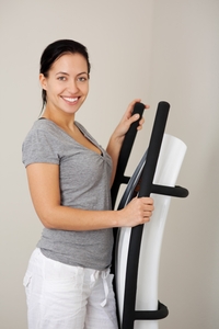 Eine Frau lächelt in die Kamera und hält die Hände an den Griffen einer Vibrationsplatte fest.