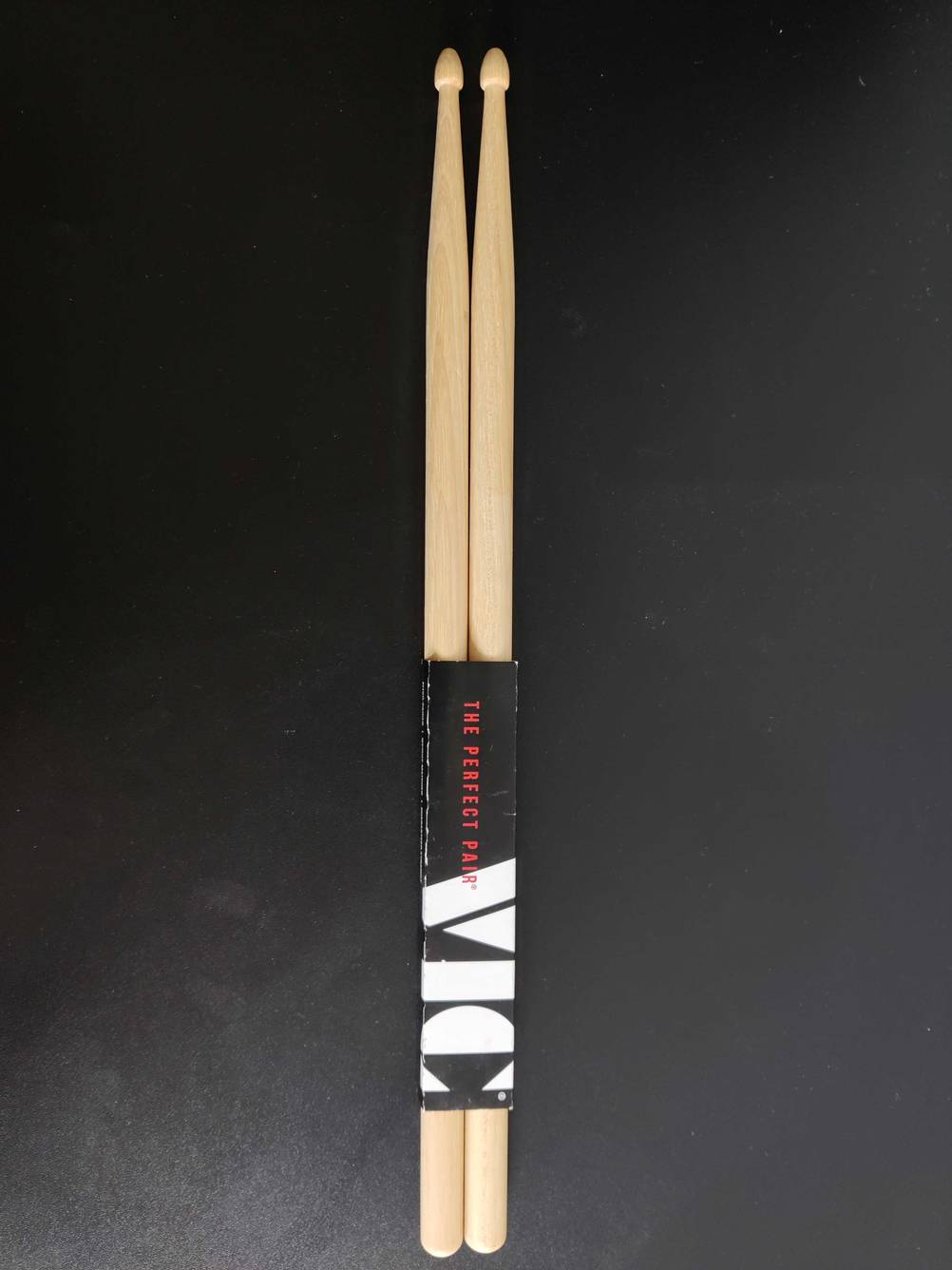 Im Test: Ein Paar Drumsticks in Originalverpackung von oben auf einer dunklen Fläche.