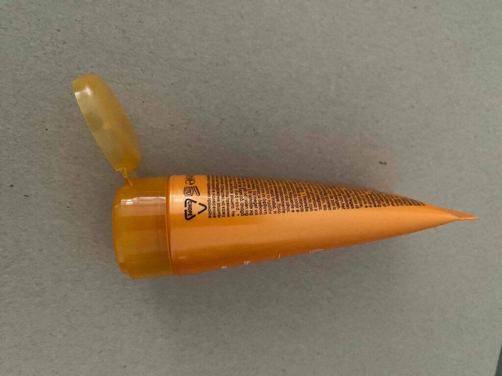 Die getestete Tagescreme mit LSF 30 in der orangefarbenen geöffneten Tube befindet sich auf einer grauen Oberfläche.
