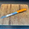 Victorinox-Brotmesser in orange auf einem Brett liegend.