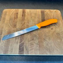 Victorinox-Brotmesser in orange auf einem Brett liegend.