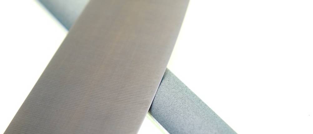 Victorinox-Messerschärfer-Test: Nahaufnahme einer Kochmesserklinge auf einem der Schärfkante eines Messerschärfers vor weißem Hintergrund.