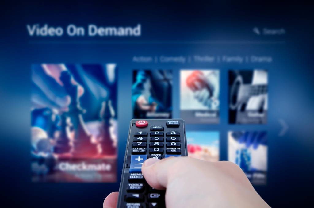 Eine Person navigiert mit einer Fernbedienung durch ein Video-On-Demand-Angebot auf einem Fernseher.