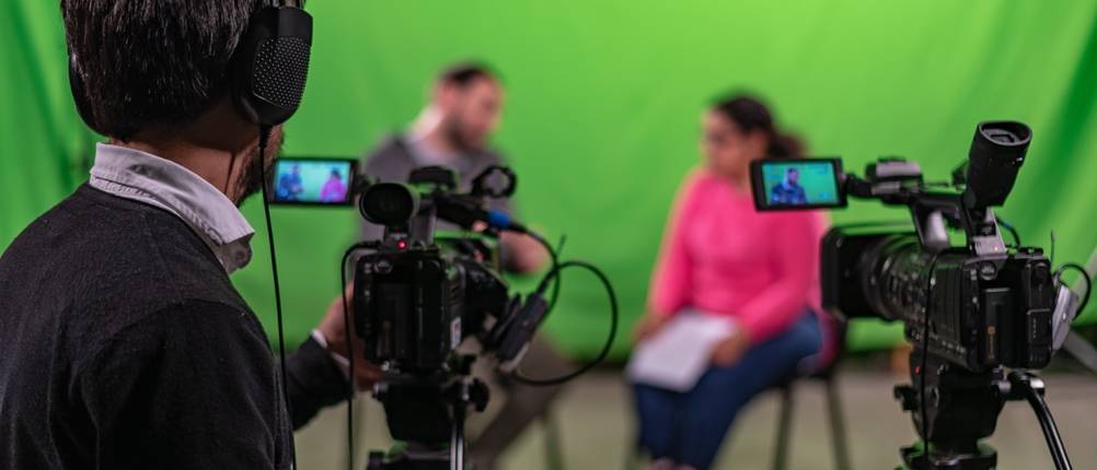 Zwei Videokameras filmen zwei Personen vor einem grünen Studiohintergrund.