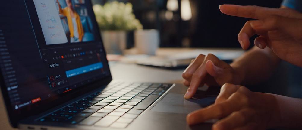 Hände bedienen einen Laptop mit geöffnetem Programm zur Videobearbeitung.